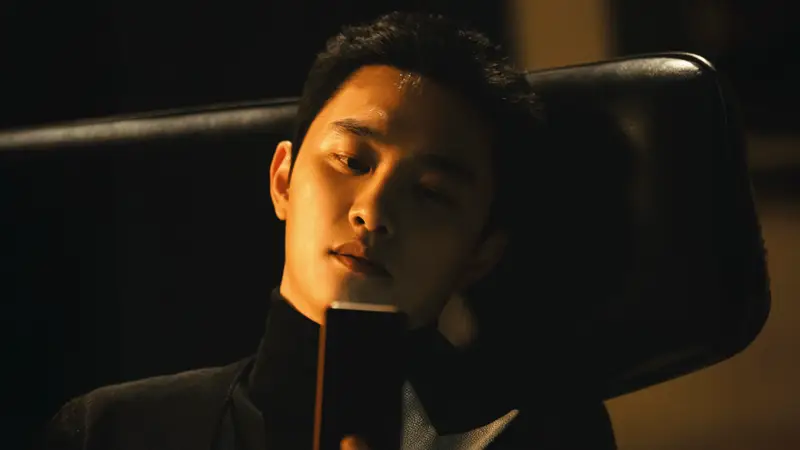 O ator Doh Kyung-soo com expressão fria em um ambiente tecnológico.