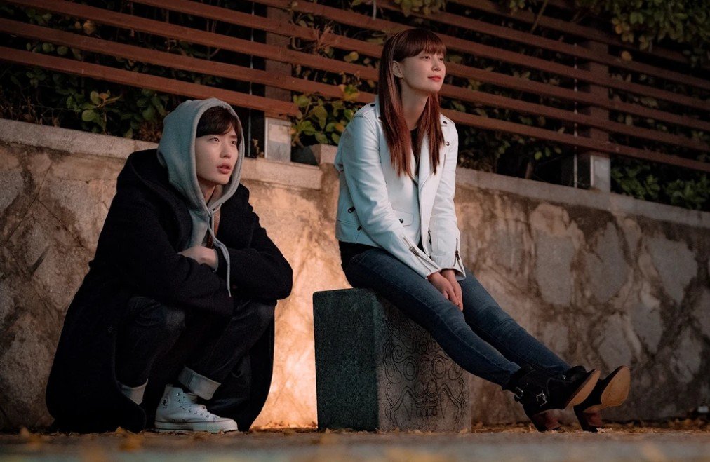 Os personagens Kang Dani e Cha Eun-ho sorrindo em um escritório repleto de livros.
