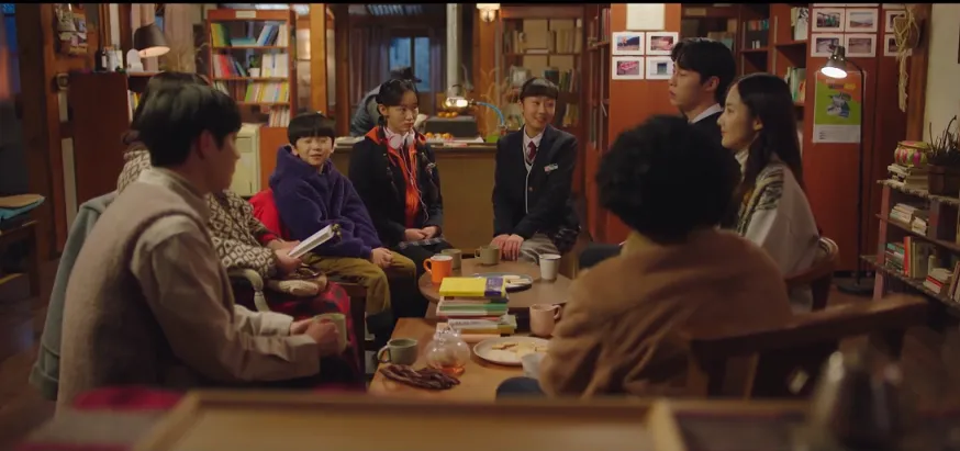 Personagens de dorama conversando calmamente em ambiente acolhedor.