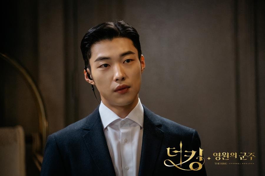  Woo Do-hwan caracterizado como o guarda-costas Jo Yeong, vestindo um terno preto impecável e segurando uma arma.