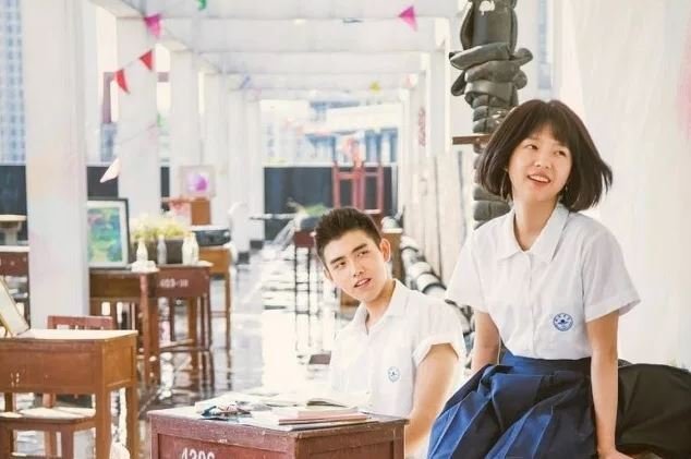 Yu Huai sorrindo com o uniforme escolar em um dia ensolarado.