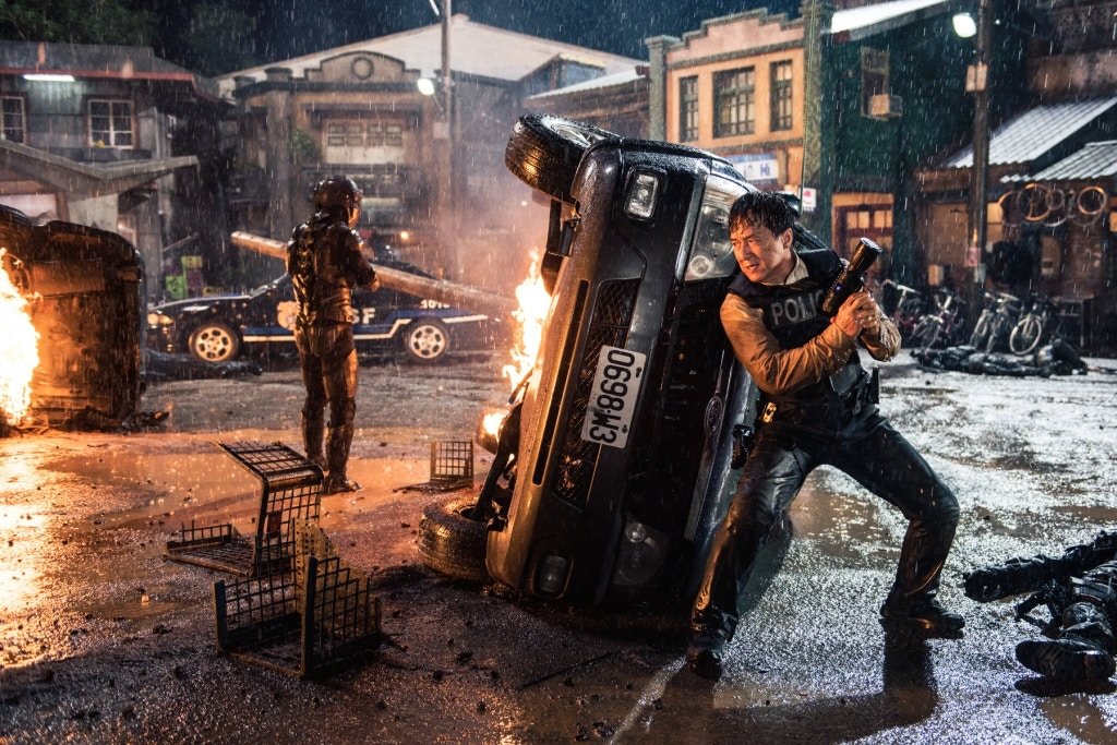 Lin Dong (Jackie Chan) protegendo a jovem Nancy em meio a uma cena de destruição no filme Inimigo.