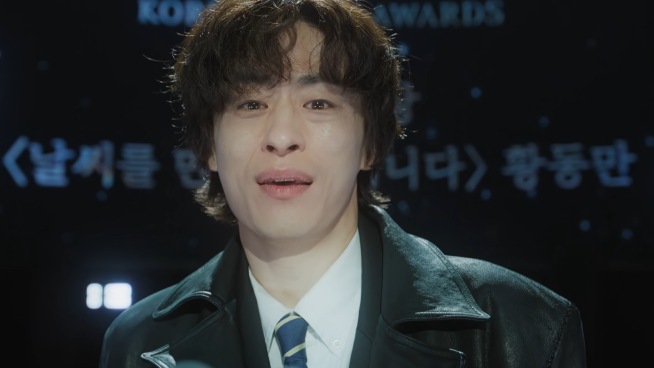 Ator Goo Gyo-hwan emocionado segurando um troféu de premiação.