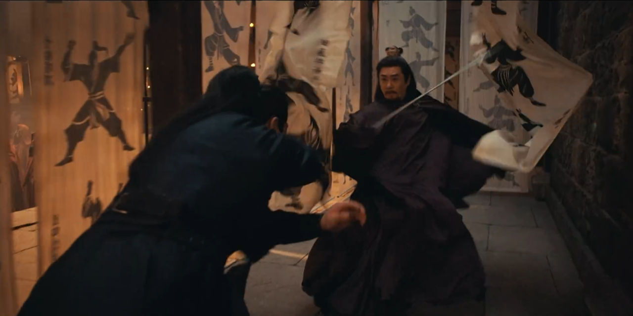 Ator chinês com capa escura e espada em um beco iluminado por tochas, com chuva caindo e expressão séria, em posição de combate.