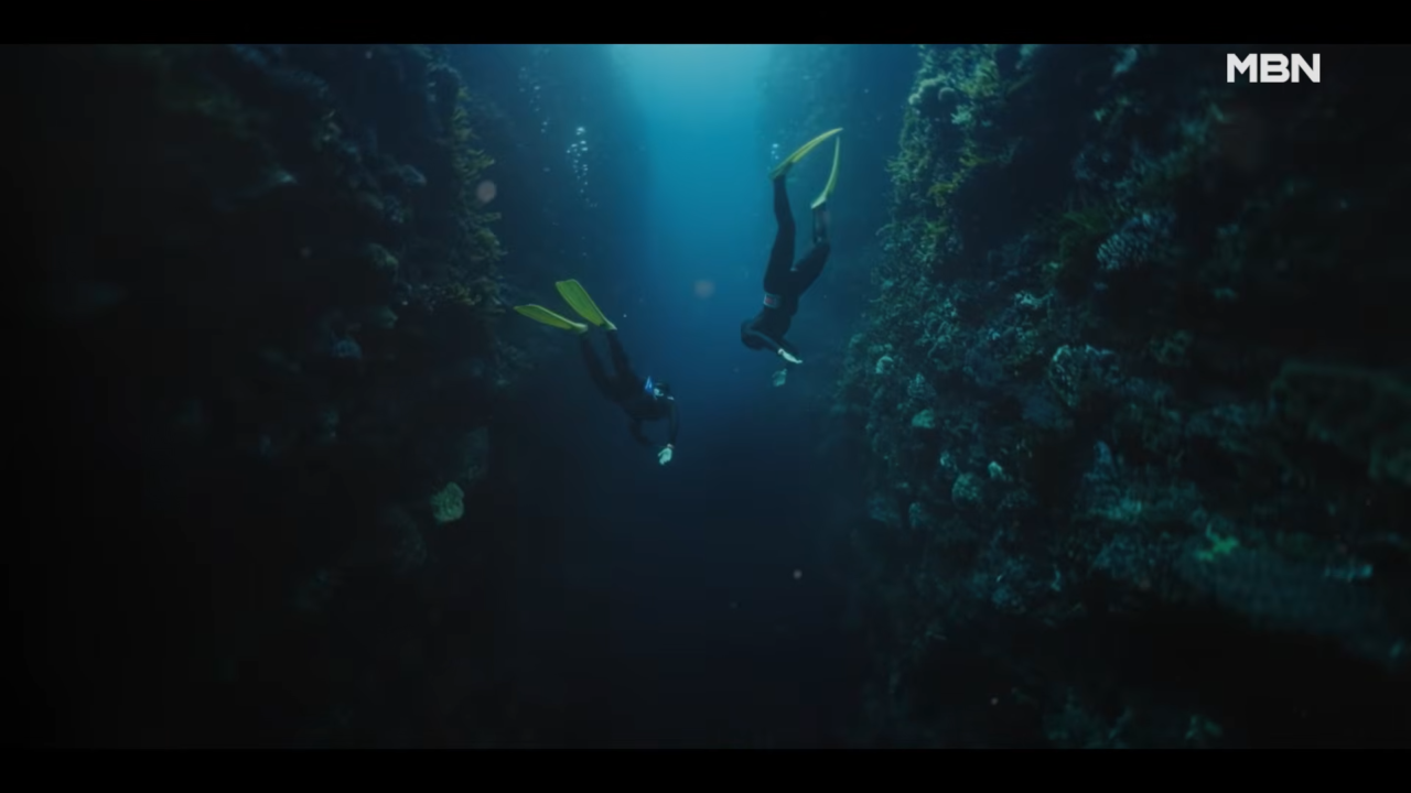 Pessoa submersa em águas azuis profundas, com raios de sol atravessando a superfície e criando um efeito de luz difusa ao redor do corpo.