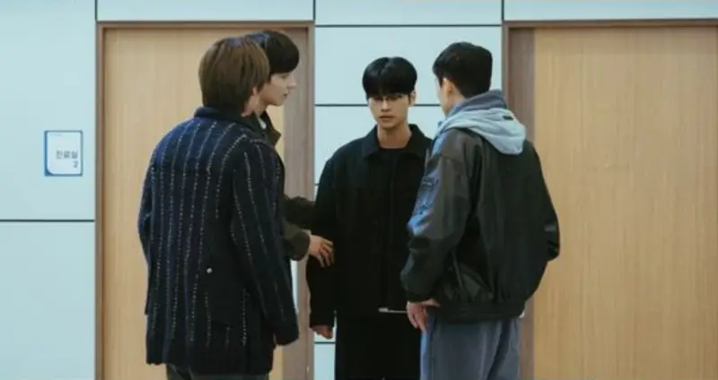 Ator sul-coreano em pé, falando para um grupo de pessoas em uma sala de reuniões.