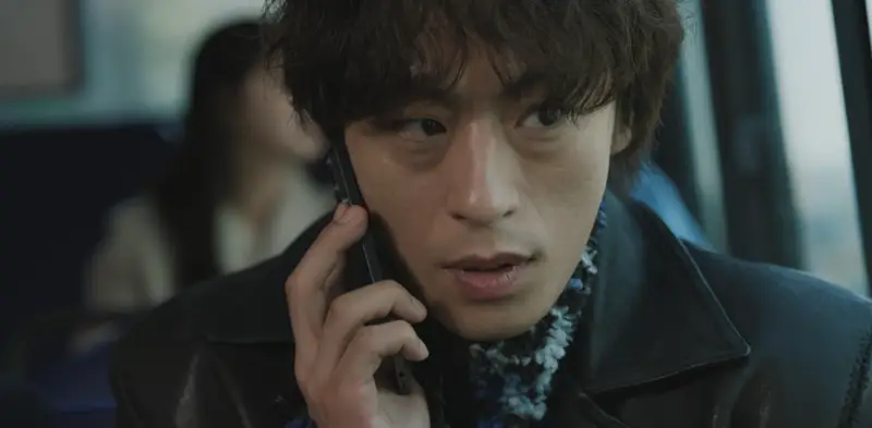 Ator sul-coreano sorrindo com o celular na mão dentro do transporte público.