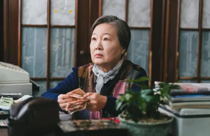 A atriz Kim Hae-sook caracterizada como Kim Jeon-bok no ambiente de seu restaurante.