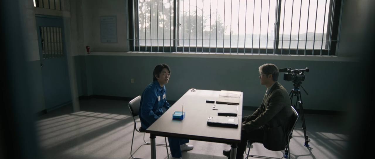 Os personagens Kang Tae Joo e Lee Gi Hwan frente a frente em uma sala de interrogatório.