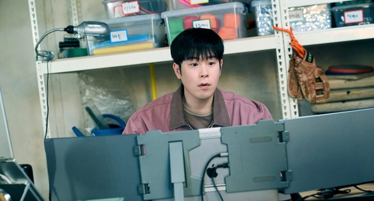 P.O do Block B atuando com expressão séria em cenário de escritório.