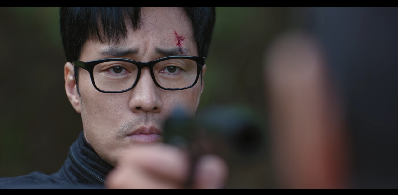 O personagem Kim olha com fúria contida enquanto é paralisado por uma ameaça inimiga no k-drama Agente Kim.