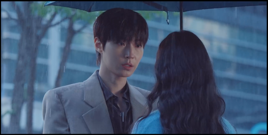 wang In Yeop segurando um guarda-chuva para proteger Lee Hyeri da forte chuva.