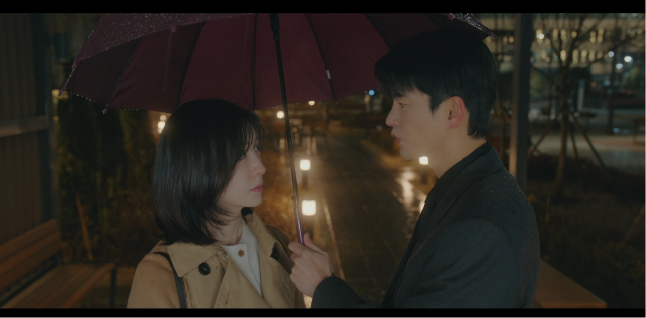 Personagem Kang Si-woo observando algo com atenção e postura séria no dorama.