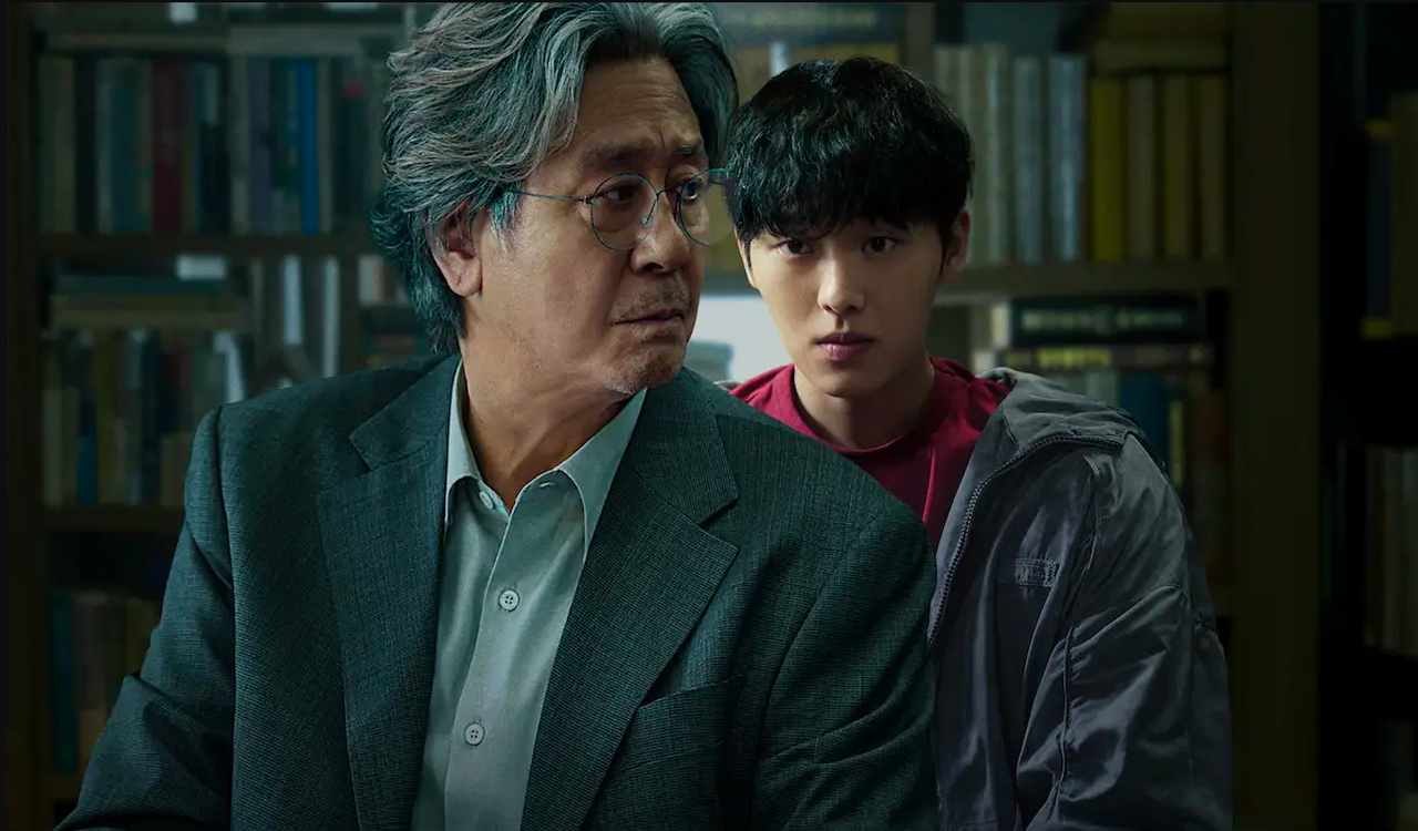 O estudante Lee Kang (Choi Hyun Wook) observando o professor com um olhar analítico e calculista, evidenciando o desequilíbrio de poder na relação]