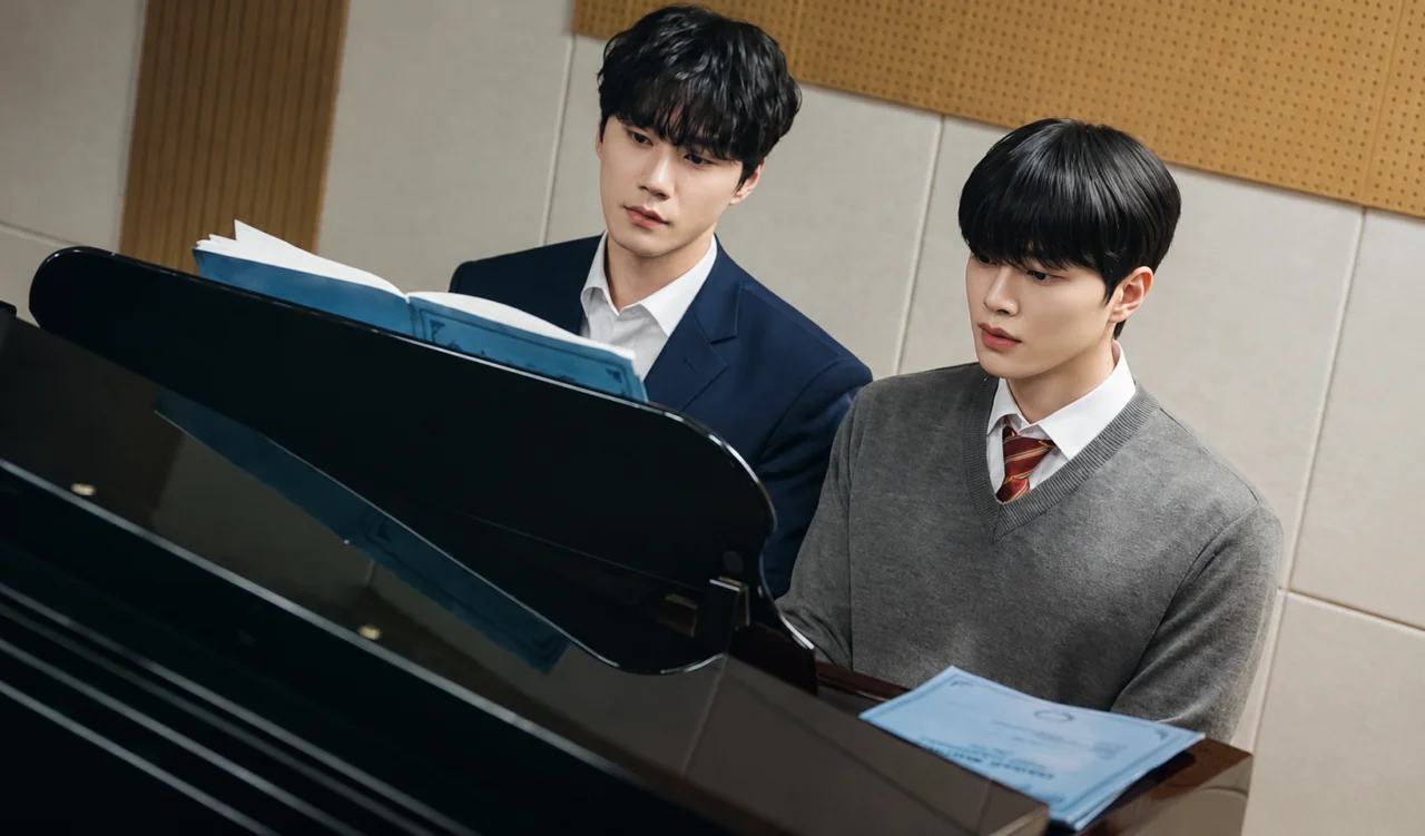 Song Kang e Lee Jun Young sentados lado a lado tocando o mesmo piano.